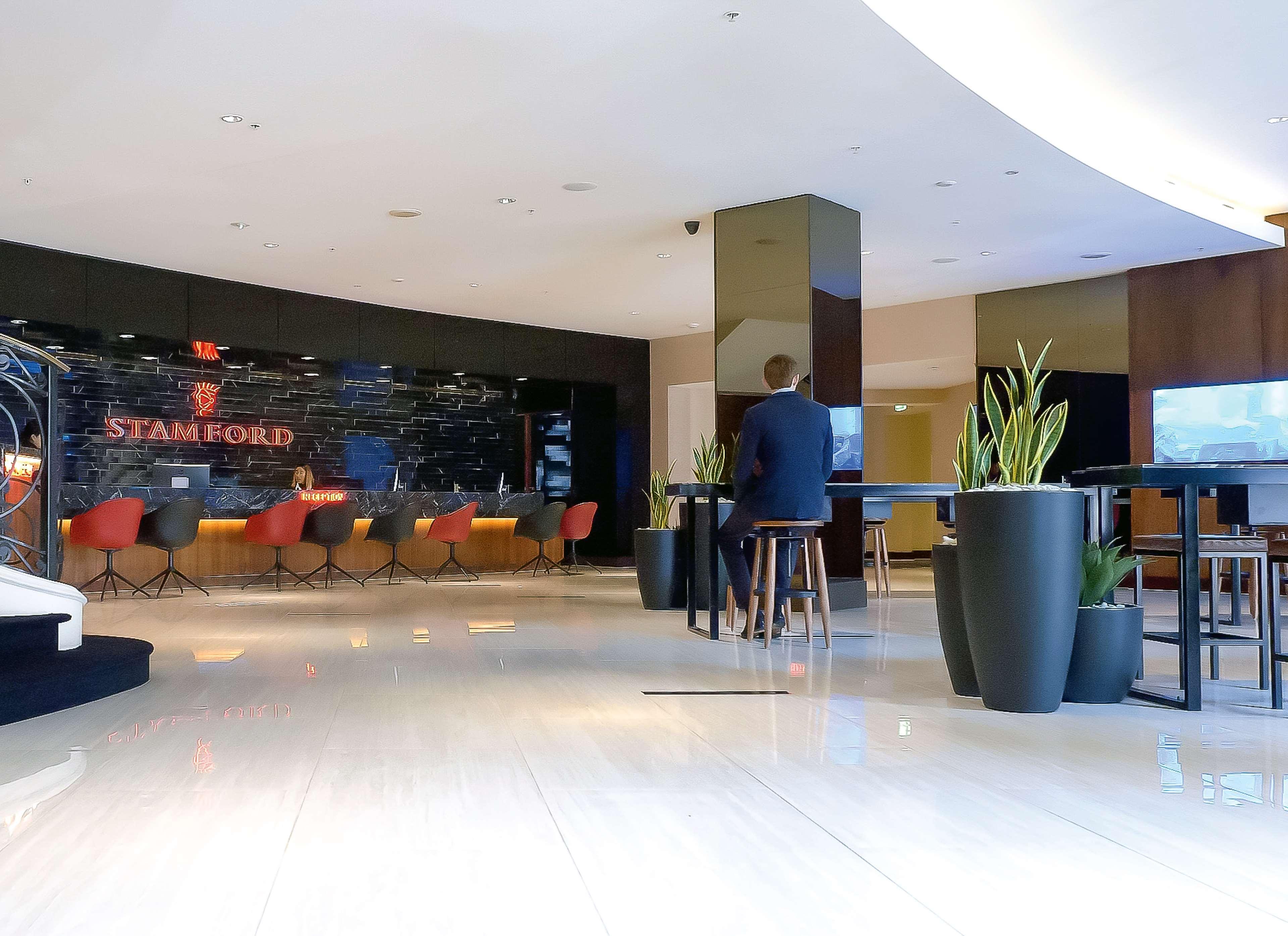 Stamford Plaza Sydney Airport Hotel & Conference Centre Exterior photo The photo shows the interior of a modern hotel lobby. In the background, there is a stylish reception area with the word "STAMFORD" prominently displayed. The seating consists of colorful chairs around tables, and the design features a sleek, contemp
